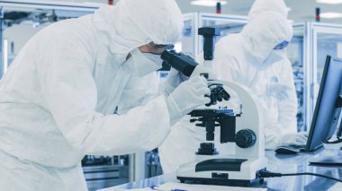 Koruyucu Giysiler Laboratuvarında Araştırma Yapan, Mikroskop kullanan ve Veri Yazan Bilimadamı. Yarı iletkenler ve İlaç Ürünleri Üreten Modern Manufactory üzerinde çalışan işçiler.