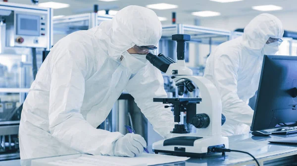 In Laboratory Scientists in Protective Clothes Doing Research, Using Microscope and Entering Data into Personal Computer. Modern Manufactory Producing Semiconductors and Pharmaceutical Items. — Stock Photo, Image