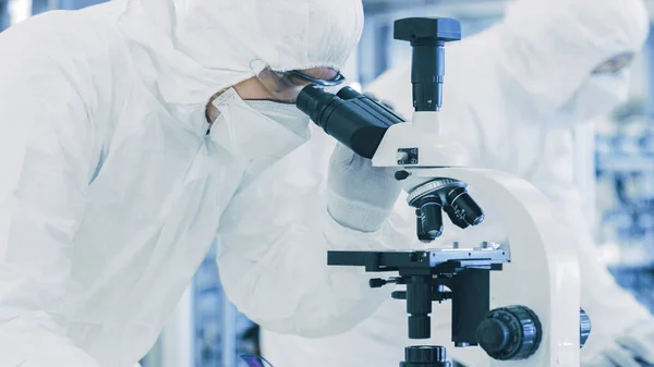 Em Laboratório Cientista em Roupas de Proteção Fazendo Pesquisa, Usando Microscópio e Escrevendo Dados. Trabalhadores que trabalham em uma manufatura moderna produzindo semicondutores e itens farmacêuticos. — Fotografia de Stock