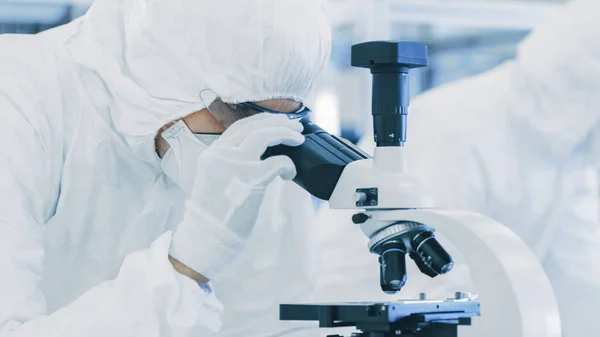 In laboratorio Scienziato in indumenti protettivi facendo ricerca, utilizzando microscopio e annotare i dati. Lavoratori che lavorano su una manifattura moderna che produce semiconduttori e articoli farmaceutici. — Foto Stock