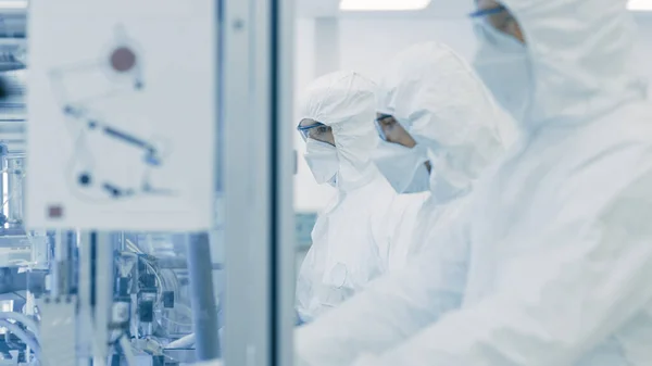 In einer Fabrik arbeiten Wissenschaftler in steriler Schutzkleidung an einer modernen industriellen 3D-Druckmaschine. Pharmazeutische, biotechnologische und Halbleiterfertigung. — Stockfoto