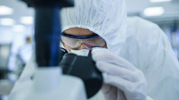 Close-up Shot of a Scientist in Protective Clothes Doing Research usa microscópio e computador pessoal em laboratório. Fabricação moderna produzindo semicondutores e itens farmacêuticos. — Fotografia de Stock