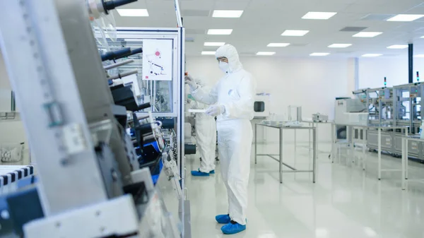 Sterile High Precision Manufacturing Laboratory where Scientists in Protective Coveralls Turn on Machninery, Use Computers and Microscopes, doing Pharmaceutics, Biotechnology and Semiconductor