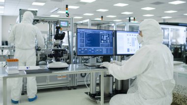 Steril Takım Elbiseli Bilim Adamlarının Bilgisayarlarla Çalışırken Çektiği Analiz Verisi Laboratuvarda Modern Endüstriyel Makineler 'i oluşturuyor. Ürün Üretim Süreci: İlaç, Yarı iletkenler