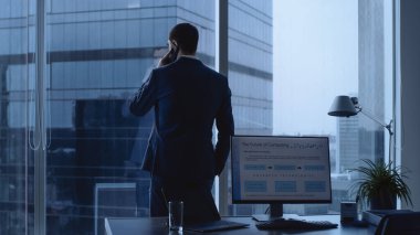Ofisinde takım elbiseli kendine güvenen bir işadamı pencereden dışarı bakıyor ve anlaşmayı tamamlamak için önemli bir telefon görüşmesi yapıyor. Kişisel Bilgisayarlı Masa Analitik Grafikleri Gösterir