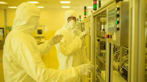 Team of Scientists in Sterile Protective Clothing Work on a Modern Industrial 3D Printing Machinery. Pharmaceutical, Biotechnological and Semiconductor Creating Manufacturing Process. Yellow Filter.