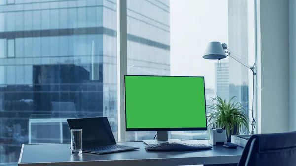 Zdjęcie z biurka z zielonym monitorem na którym stoi komputer osobisty. Nowoczesny stylowy pokój z widokiem na dzielnicę biznesową Big City. — Zdjęcie stockowe