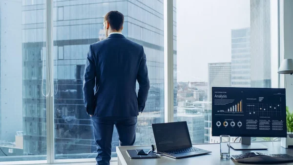 Självsäker affärsman i en kostym överväger Business Deal i sitt kontor, tittar ut genom fönstret. Fönstret har panoramautsikt över storstadens affärsdistrikt. — Stockfoto