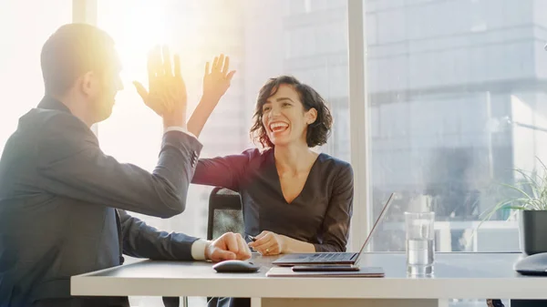 Top-Managerinnen und männliche Geschäftsleute sitzen am Schreibtisch und machen High Five, nachdem sie eine erfolgreiche Lösung für das Problem gefunden haben. Schöne Menschen in modernen Büros mit Großstadtblick. — Stockfoto