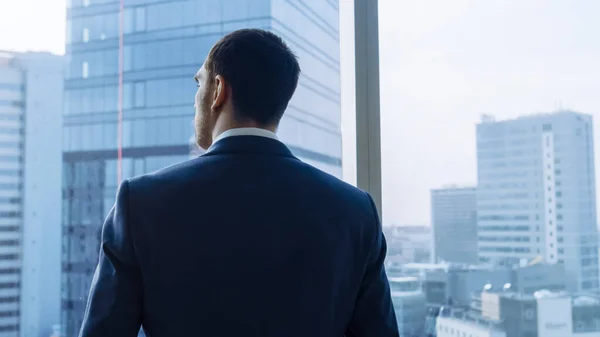 Medium skott av framgångsrik affärsman bär en kostym stående i sitt kontor, Kontemplera nästa stora affär, tittar ut genom fönstret. Storstadens affärsdistrikt panoramafönster Visa. — Stockfoto