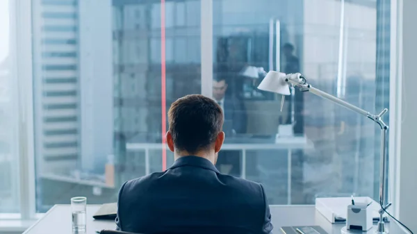 Voltar Visão de Empresário Confiante Sentado em Sua Mesa e Trabalhando em um Laptop, Homem Corporativo de Sucesso Fazendo um Trabalho Importante. Ambiente de escritório moderno tem janela com vista para o distrito de negócios da cidade grande. — Fotografia de Stock