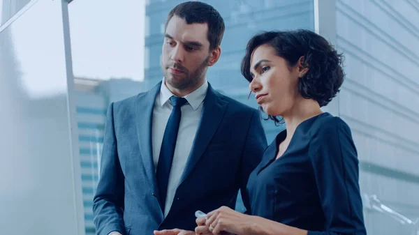 En la oficina Hombre de negocios guapo y hermosa empresaria Piense en los planes de futuro Escrito en la pizarra blanca. Planificación de la expansión de marcas, consultoría de datos y creación de gráficos. Gente moderna con estilo. — Foto de Stock