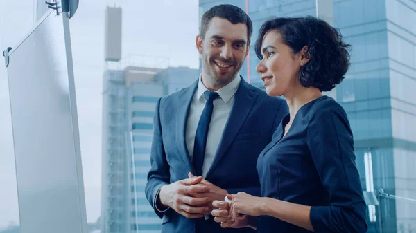 Dans le bureau bel homme d'affaires et belle femme d'affaires ont une discussion tout en utilisant le tableau blanc. Planning Marking Expansion, Consulting Data and Making Graphs. Des gens modernes et élégants. — Photo