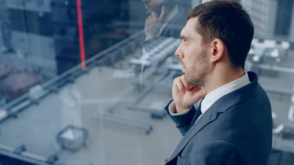 Itsevarma liikemies puvussaan seisoo toimistossaan, katselee ikkunasta ja soittaa tärkeän puhelun, jotta hän voi sulkea sopimuksen. Taustalla Näkymä Big City. — kuvapankkivalokuva
