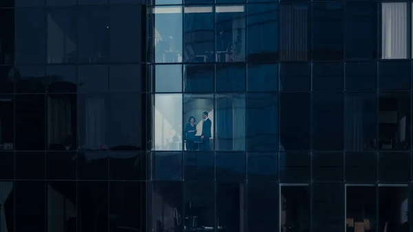 Aerial Shot From Outside: Businessman and Businesswoman Talking Business while Standing next to Skyscraper Office Window. Shot of the Financial Business District of the Big City. — Stock Photo, Image