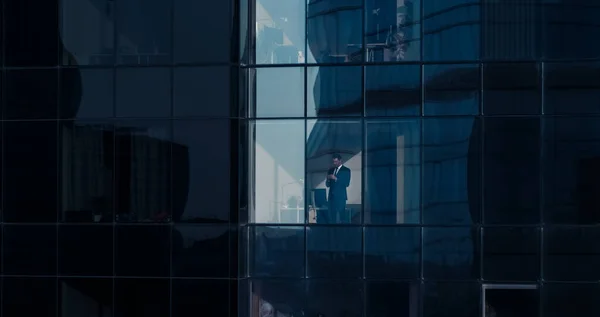 Aerial View Shot: From Outside into Office Building with Businessman Using Mobile Phone and Standing Next to the Office Window. Beautiful Shot of The Financial Business District Skyscrapers. — Stock Photo, Image