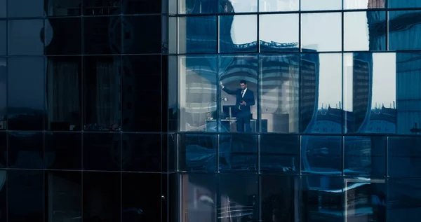 Vue Aérienne : De l'extérieur dans un immeuble de bureaux avec un homme d'affaires utilisant un téléphone portable et debout à côté de la fenêtre de bureau. Magnifique prise de vue des gratte-ciel du Financial Business District. — Photo