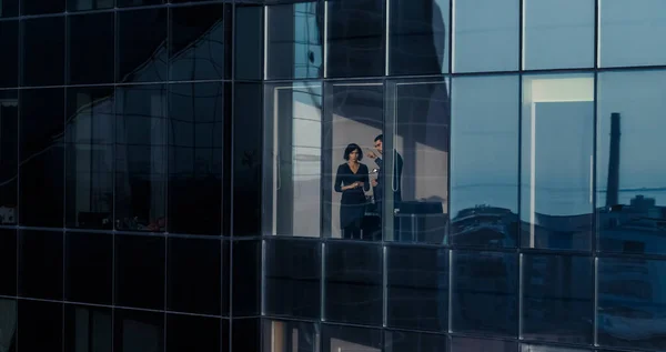 Strzał z powietrza spoza drapacza chmur: Biznesmen i Bizneswoman rozmawiają o interesach stojąc przy oknie biura. Shot of Financial Business District i przedsiębiorców pracujących w — Zdjęcie stockowe