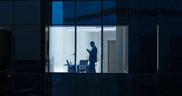 Tiro aéreo: De fora para o prédio do escritório com empresário usando telefone celular e em pé pela janela do escritório. Lindo tiro dos arranha-céus do Distrito Financeiro de Negócios. — Fotografia de Stock