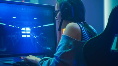 Kişisel bilgisayarında FPS Video Oyunu 'nda oynayan Güzel Profesyonel Oyuncu Kız' ın, Gözlük ve Kulaklık takan Sevimli İnek 'in çekimleri. Neon Room. Çevrimiçi Sanal Oyunlar İnternet Şampiyonası Etkinliği.