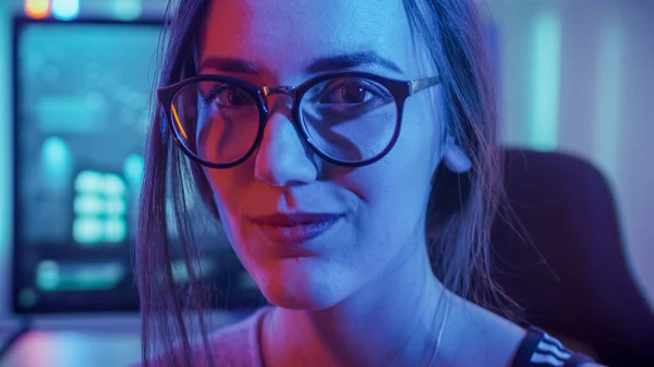 Retrato de la hermosa joven jugadora profesional sentada en su computadora personal y mira a la cámara. Atractivo geek chica jugador usando gafas en la habitación Lit por luces de neón. —  Fotos de Stock