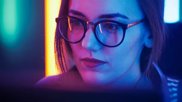 Retrato de la hermosa joven sentada delante de la computadora, navegando en Internet, jugando juegos en línea, streaming. Chicas lindas con gafas en la habitación Cool Retro Neon Lit. — Foto de Stock