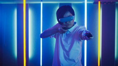 Doğu Asya Pro Oyuncuları Sanal Gerçeklik Kulaklığı Giyerek Oyun Online Video Oyun Oynayıcı, Joystick Kontrolörlerini Shotgun Gun olarak kullanıyor. Soğuk Retro Neon Renkleri Odada.