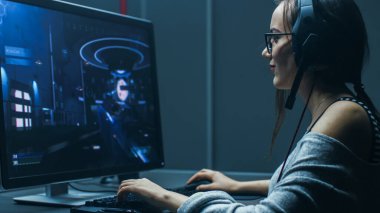 Shot of the Beautiful Professional Gamer Girl Playing in First-Person Shooter Online Video Game on Her Personal Computer. Casual Cute Geek wearing Glasses and Talking into Headset. In the Basement clipart