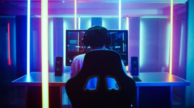 Back View Shot of the Beautiful Professional Gamer Girl Putting on Headset and Starts Playing Online Video Game on Her Personal Computer. Cute Casual Geek Girl. Room Lit by Neon Lamps in Retro Arcade clipart