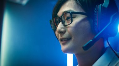 Çevrimiçi Video Oyunu 'nda oynayan Asyalı profesyonel oyuncunun yakın plan portresi, gözlük takan Hes, kulaklıkla takım arkadaşlarıyla sohbet ediyor. Neon renkli oda. eSport Siber Oyunları