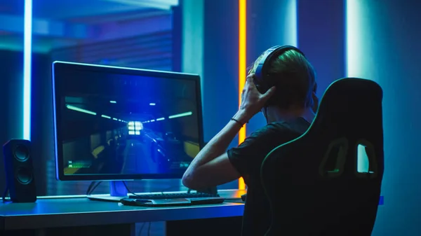 Pro Gamer juega en la primera persona Shooter en su ordenador personal. Se pone los auriculares. Habitación de color neón. Torneo de eSport en línea en acción. Disparo en lente anamórfica. —  Fotos de Stock