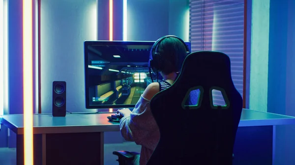 Menina Gamer profissional bonita jogando em primeira pessoa Shooter Online Video Game em seu computador pessoal. Casual bonito Geek Girl usando fone de ouvido. escuro quarto de repente lit por luzes de néon em retro — Fotografia de Stock