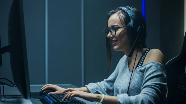 Schöne professionelle Spielerin, die in Ego-Shooter Online-Videospiel auf ihrem Personal Computer spielt. Casual Cute Geek Girl trägt Headset. Im unterirdischen Spielclub. — Stockfoto