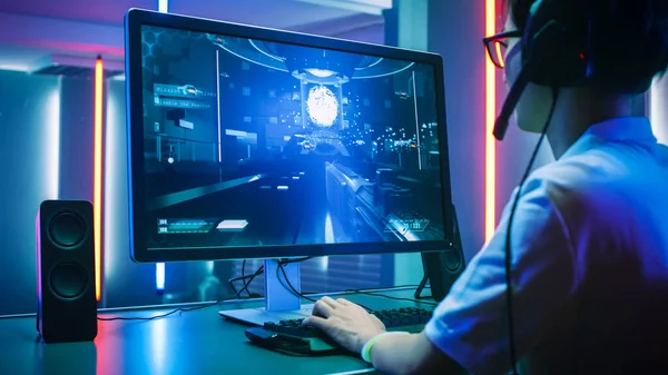 Back View Shot of Professional Gamer Playing in First-Person Shooter Online Video Game on His Personal Computer. Hes Talking with His Team Through Headset. Room Lit by Neon Lights in Retro Arcade — Stock Photo, Image