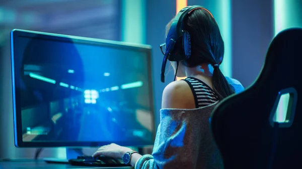 在她的个人电脑上玩FPS视频游戏的漂亮职业游戏女孩，戴着眼镜和耳机的即兴可爱极客被枪击中。尼昂房间。网上游戏及互联网锦标赛. — 图库照片