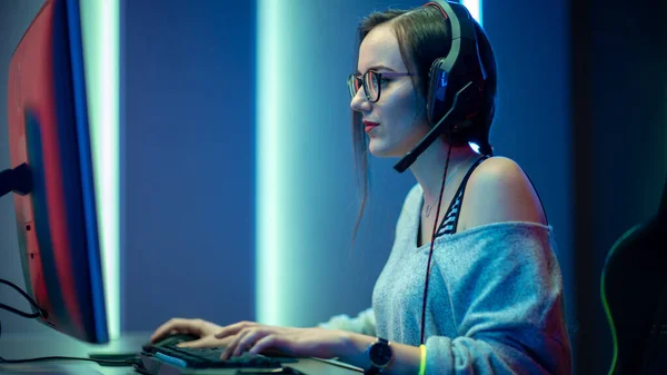 Hermosa Chica Gamer Profesional Jugando en Primera Persona Shooter Videojuego en línea en su ordenador personal. Casual lindo geek usando gafas y sonriendo. Cyber e-Sport Campeonato de Internet. —  Fotos de Stock