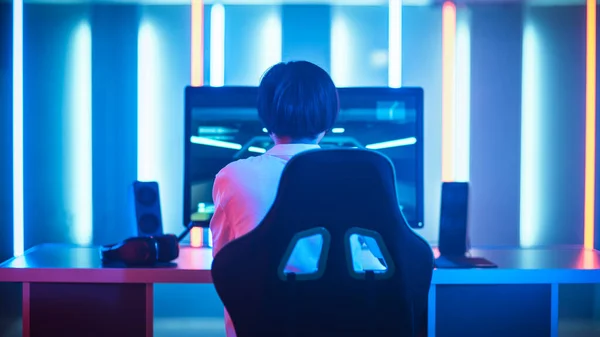 在第一人称射击在线视频游戏中，职业游戏玩家在他的个人计算机上的游戏和赢球。他正通过耳机与他的团队交谈。复古拱廊风格的霓虹灯下的房间 — 图库照片