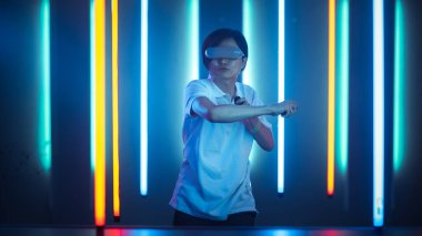 Sanal gerçeklik kulaklığı takan Doğu Asya Pro Oyuncuları Oyun Oynayıcı olarak Joystick Kontrolörleri 'ni kullanıyor. Soğuk Retro Neon Renkleri Odada.