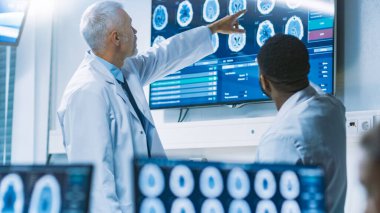 Beyin Araştırma Laboratuvarı 'nda Bilim Adamları Ekibi, Duvar TV Monitöründe Beyin Taramaları Gösterisini tartışıyor. Nörologlar etrafı monitörlerle çevrili, tomografi ve MRI taramaları gösteriyor..