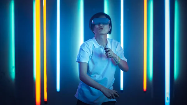 East Asian Pro Gamer Nošení Virtuální Reality Headset hraje Online videohry Shooter pomocí Joysticks Controllers jako meče. Cool Retro neonové barvy v místnosti. — Stock fotografie