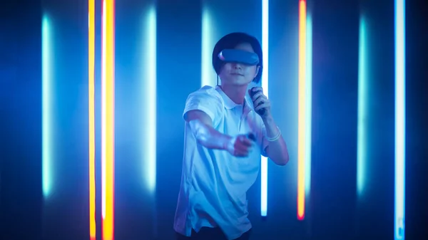 East Asian Pro Gamer Wearing Virtual Reality Headset Plays Online Video Game Shooter using Joysticks Controllers as Swords. Cool Retro Neon Colors in the Room. — Stock Photo, Image