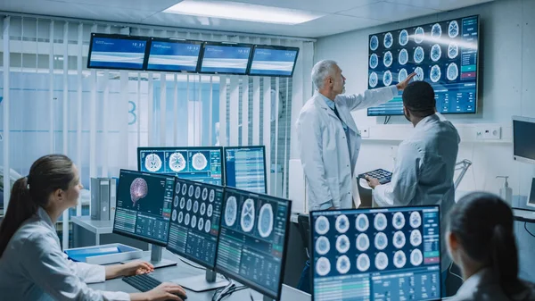 Team av professionella medicinska forskare arbetar i hjärnforskningslaboratoriet. Neurologer Neuroforskare Omgivna av monitorer som visar datortomografi, MRT-bilder som diskuterar och arbetar med personliga frågor — Stockfoto