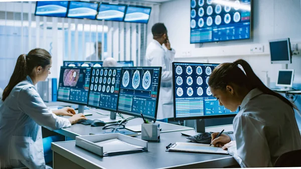 Ομάδα επαγγελματιών επιστημόνων εργάζονται στο Εργαστήριο Έρευνας Εγκεφάλου. Νευρολόγοι Νευροεπιστήμονες Περιτριγυρισμένοι από Οθόνες Εμφάνιση CT, MRI Scans Έχοντας συζητήσεις και δουλεύοντας σε προσωπικούς υπολογιστές. — Φωτογραφία Αρχείου