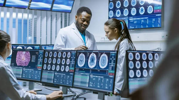 脳科学研究室では神経生理学プロジェクトの進捗状況について議論しています。MRIを示す画面に囲まれた神経科学者, CT脳スキャン画像. — ストック写真
