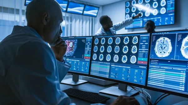 Au-dessus de l'épaule prise de vue d'un scientifique médical principal travaillant avec CT Brain Scan Images sur un ordinateur personnel en laboratoire. Les neurologues du centre de recherche travaillent sur la guérison des tumeurs cérébrales. — Photo