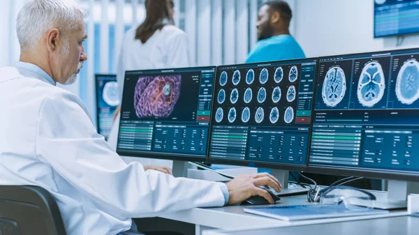 Досвідчений старший науковий співробітник працює з CT MRI Brain Scan Images on a Personal Computer in Laboratory. Неврологи в медичному дослідницькому центрі працюють над лікуванням мозкових пухлин. — стокове фото