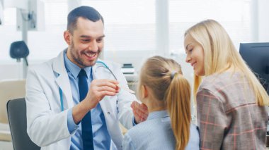Dost canlısı doktor küçük kızların boğazını kontrol ediyor. Annesi destek için burada. Modern Sağlık Hizmetleri, Arkadaş canlısı Pediyatrist ve Parlak Ofis.