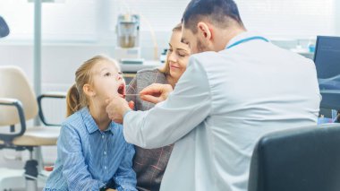 Dost canlısı doktor küçük kızların boğazını kontrol ediyor. Annesi destek için burada. Modern Sağlık Hizmetleri, Arkadaş canlısı Pediyatrist ve Parlak Ofis.