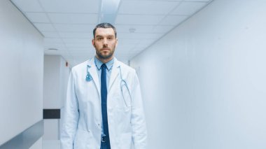 Hastane koridorunda steteskopla yürüyen kararlı, yakışıklı doktor, beyaz önlüklü. Profesyonel Personelle Modern Parlak Klinik.