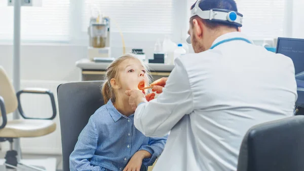 Vriendelijke dokter checkt kleine meisjes pijnlijke keel, genezende griep. Moderne Medische Gezondheidszorg, Vriendelijk Kinderarts en Helder Bureau. — Stockfoto